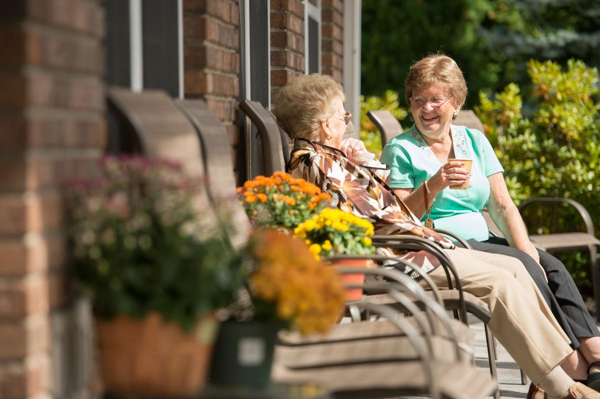 Two senior women enjoying a conversation on a sunny day, surrounded by flowers.