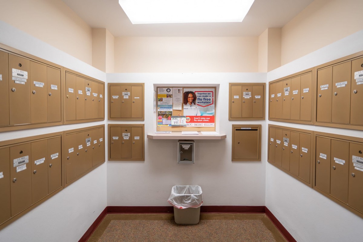 A small mail room with multiple mailboxes lining the walls and a recycle bin in the center.