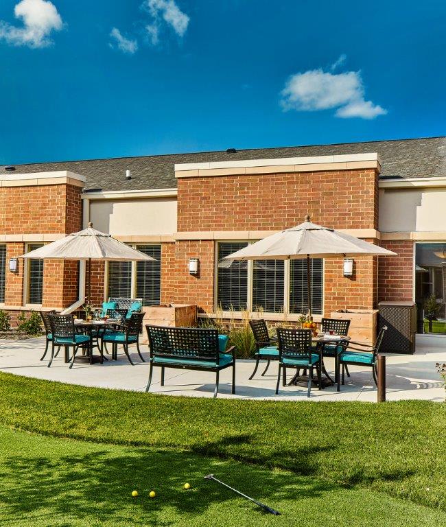 A sunny patio with outdoor seating and umbrellas in front of a brick building.