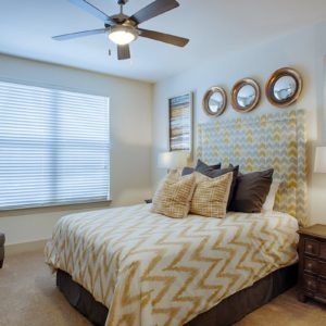 A modern bedroom featuring stylish bedding with chevron patterns, complemented by artwork above the headboard and a ceiling fan for comfort.