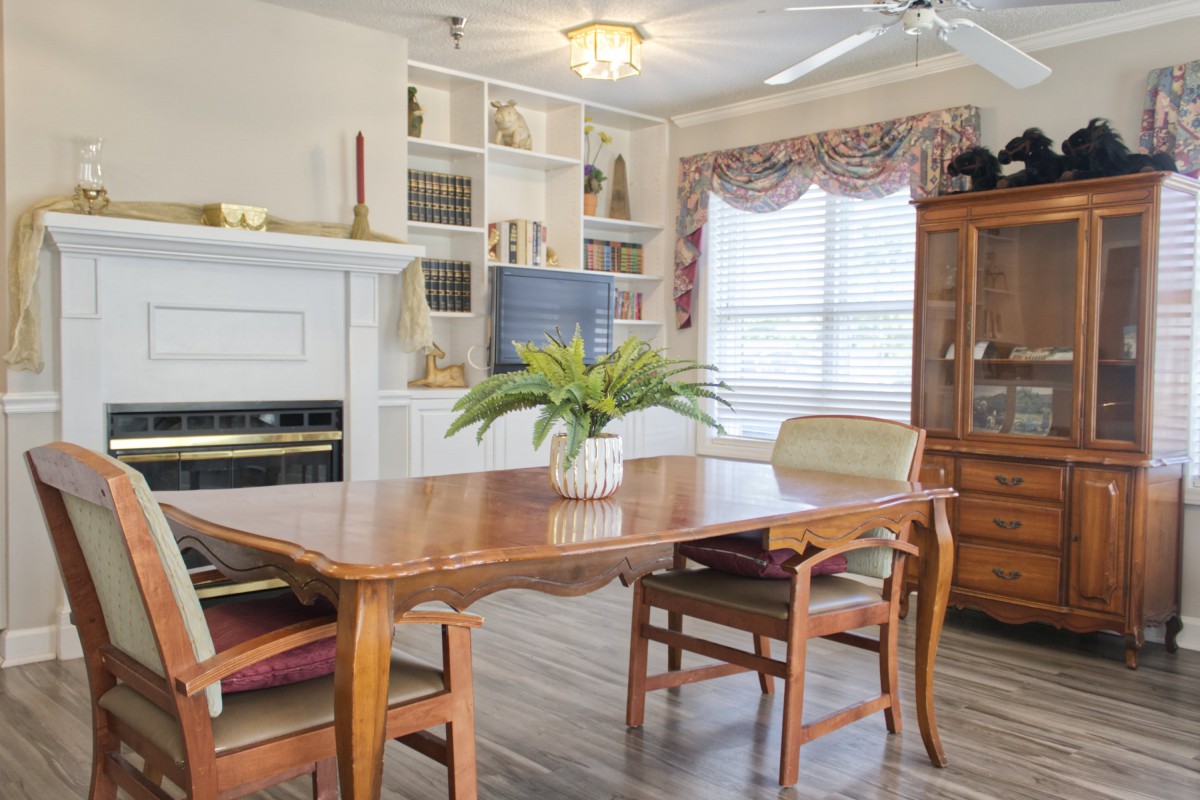 A cozy dining room with a wooden table, chairs, and decorative elements including a fireplace and bookshelves.