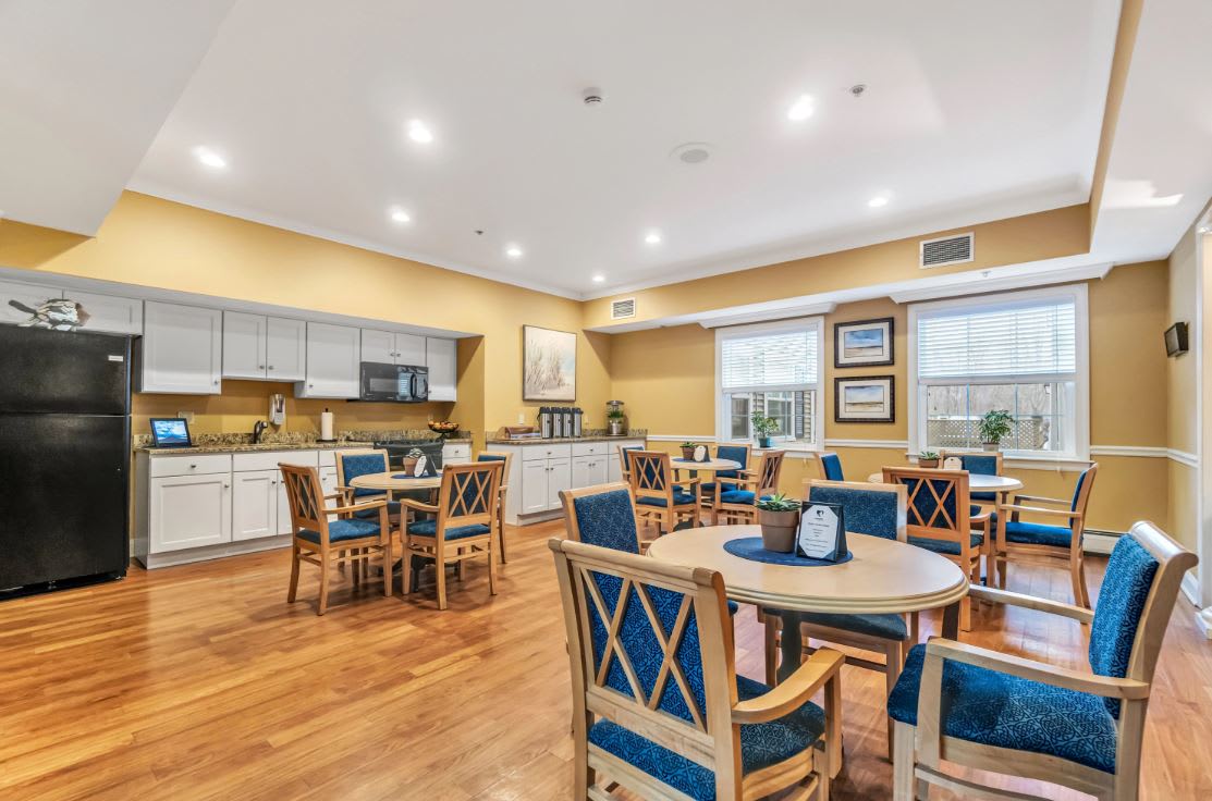 A cozy dining area with wooden floors, tables, and chairs, adjacent to a modern kitchen.