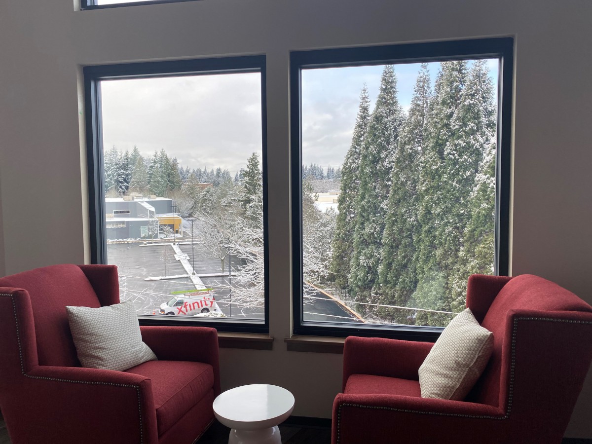 A cozy seating area with red chairs overlooks a snowy landscape through large windows.