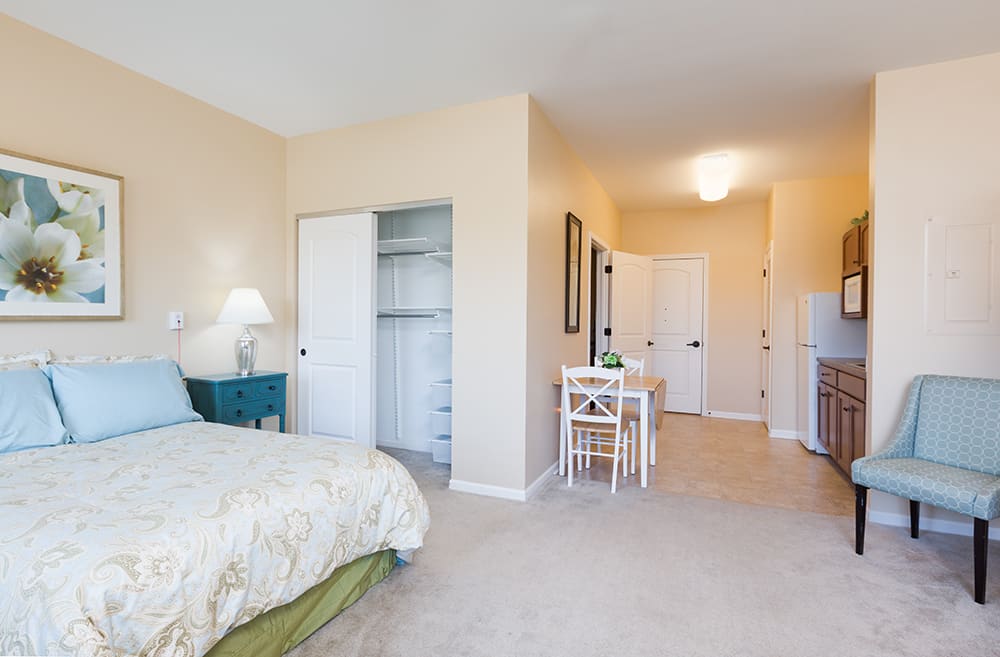 A minimalist bedroom with a bed, open closet, and small dining table.