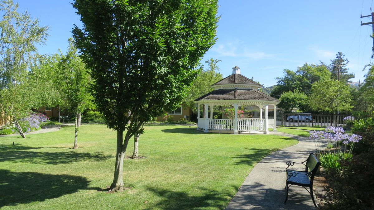 A scenic park with a gazebo, lush green grass, and trees under a clear blue sky.