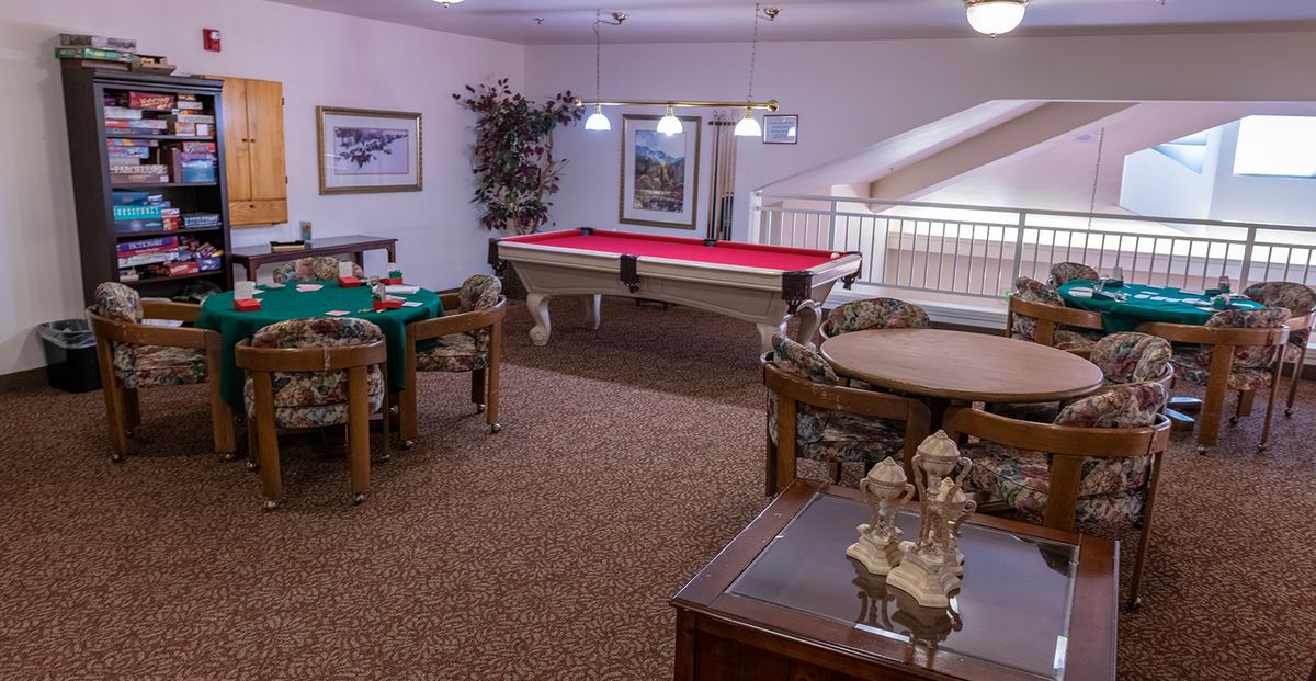 A cozy game room featuring a billiards table and card tables, complete with elegant lighting and decor.