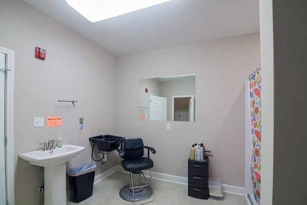 Interior of a small barbershop or salon with a chair, sink, and mirror.