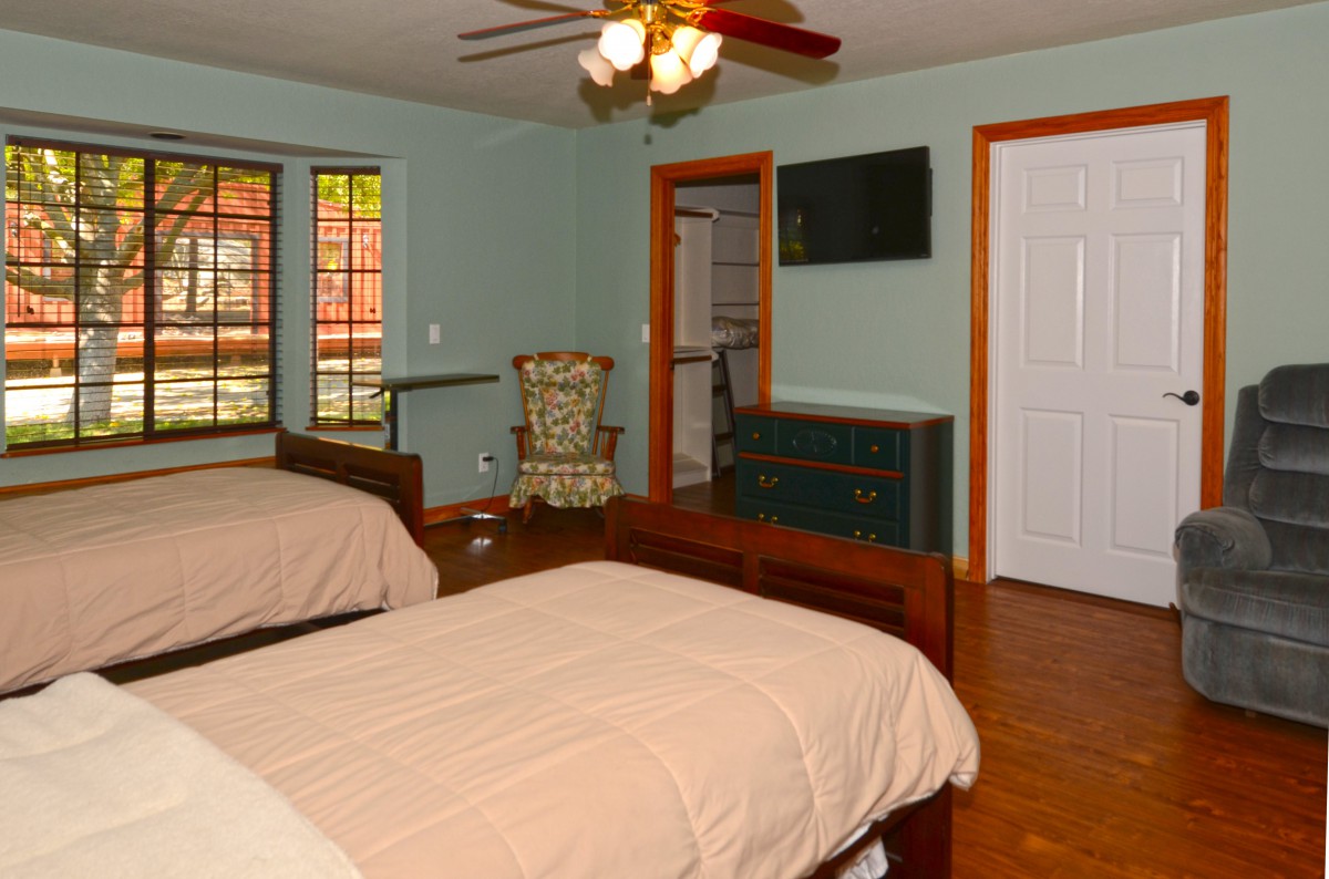 A cozy bedroom with two twin beds, a ceiling fan, and a flat-screen TV.