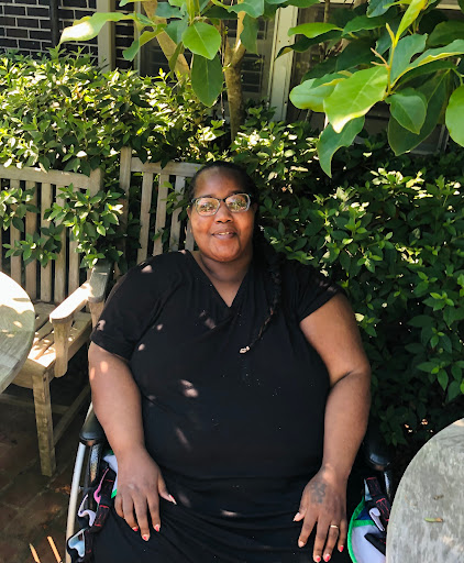 A smiling individual in a wheelchair enjoys the serene garden atmosphere.