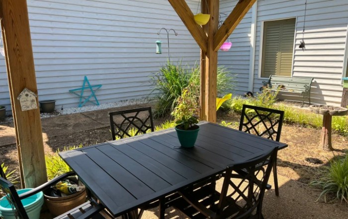 A cozy backyard patio with a wooden table and chairs under a pergola.