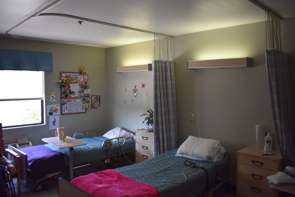 A hospital room with two patient beds, a nightstand, and curtains for privacy.