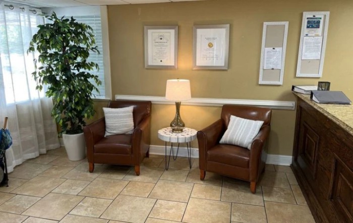 A cozy seating area with two brown leather chairs, a lamp on a small round table, and framed art on the wall.