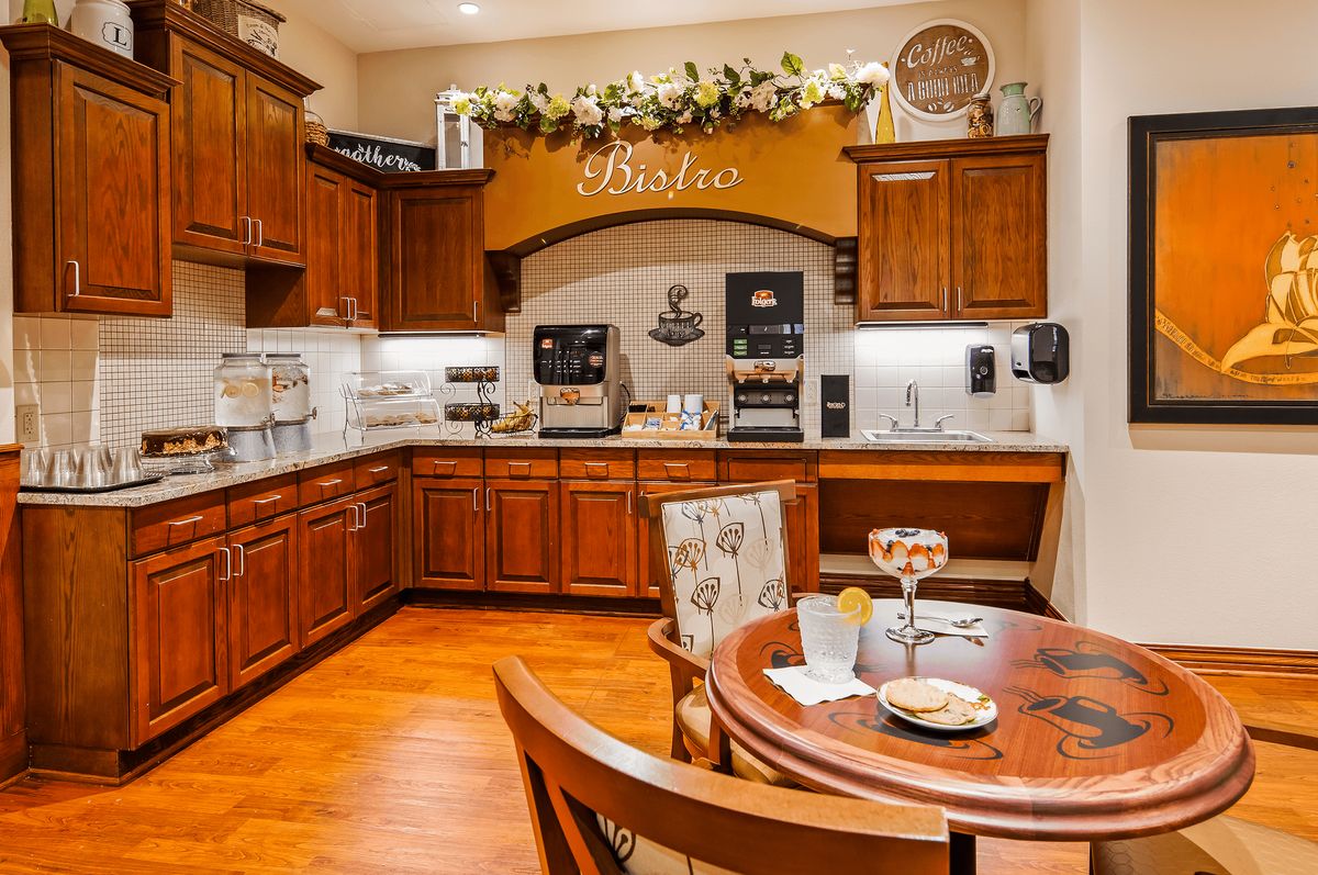 A cozy kitchen with wooden cabinets and a coffee station, featuring a small dining table set for two.