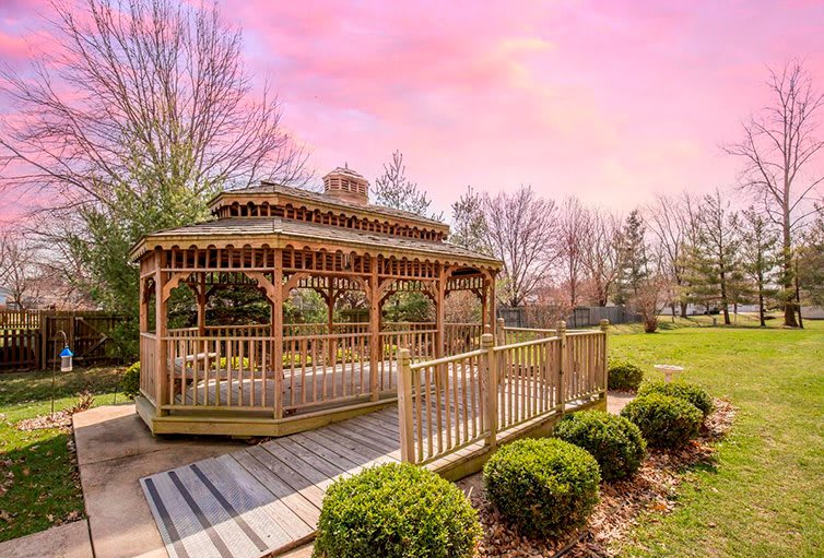 A charming wooden gazebo set in a picturesque park with a vibrant sunset sky.
