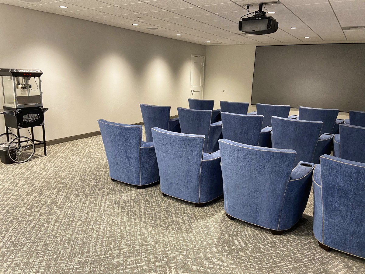 A conference room with rows of blue chairs facing a projector screen.