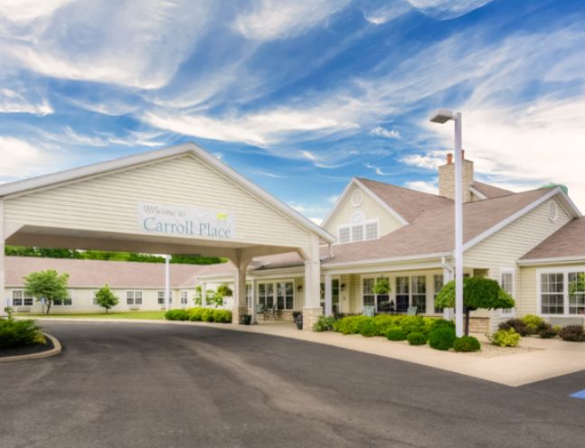 A welcoming entrance of a building with a covered driveway under a partly cloudy sky.