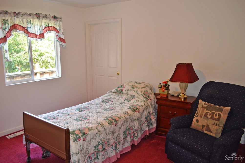 A cozy bedroom with a single bed, nightstand, and a chair by the window.