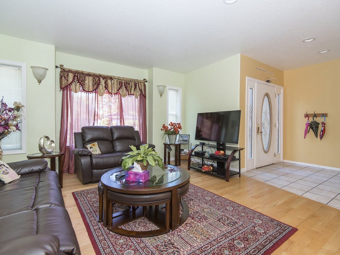 A cozy living room featuring leather sofas, a wooden coffee table, and a television set, accented with a patterned rug and elegant curtains.