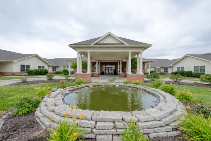 A building entrance with a landscaped pond and columns under a cloudy sky.