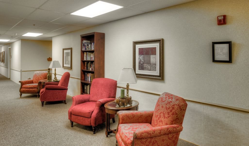 A cozy interior with red armchairs, a wooden bookshelf, and framed artwork on the wall.