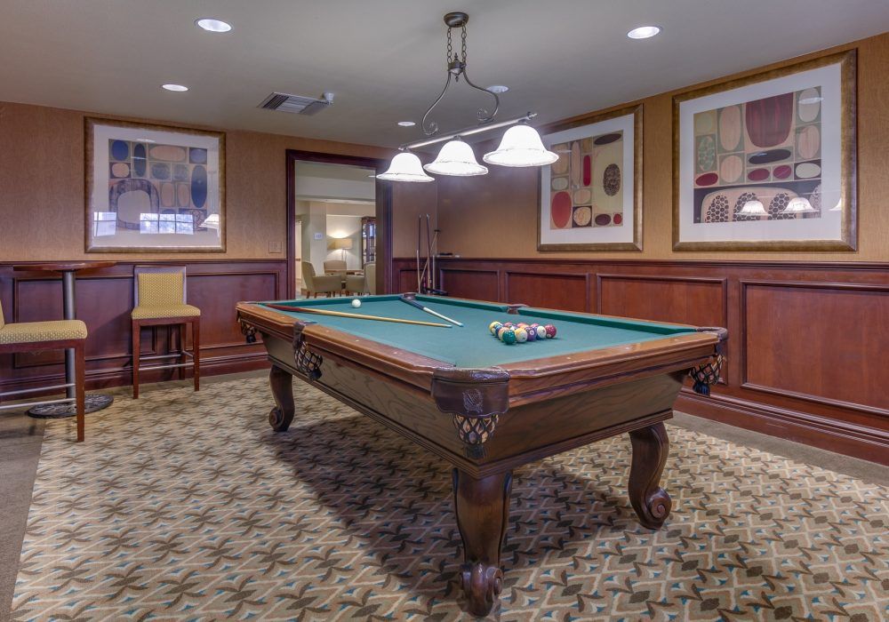 A cozy game room featuring a pool table under warm lighting with wood paneling and framed artwork on the walls.