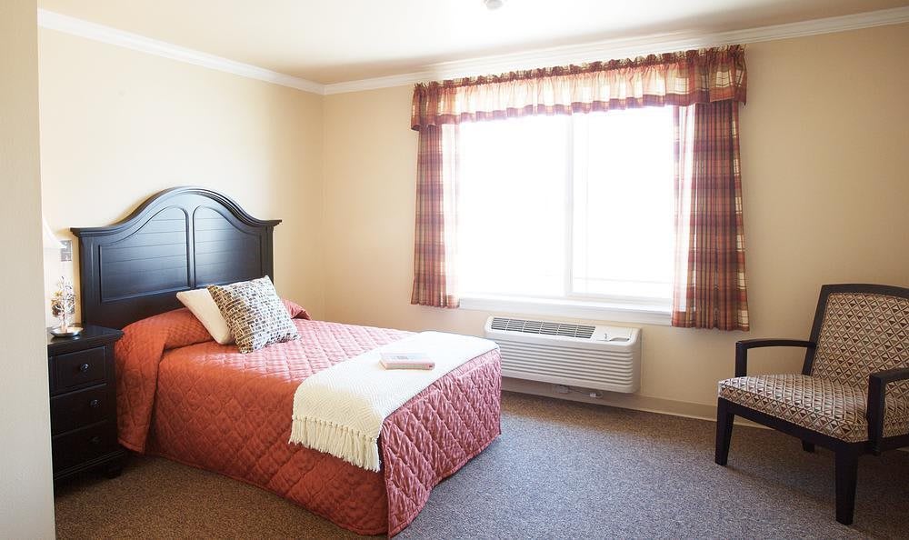A well-lit hotel bedroom featuring a single bed with decorative pillows, a large window, and simple decor.