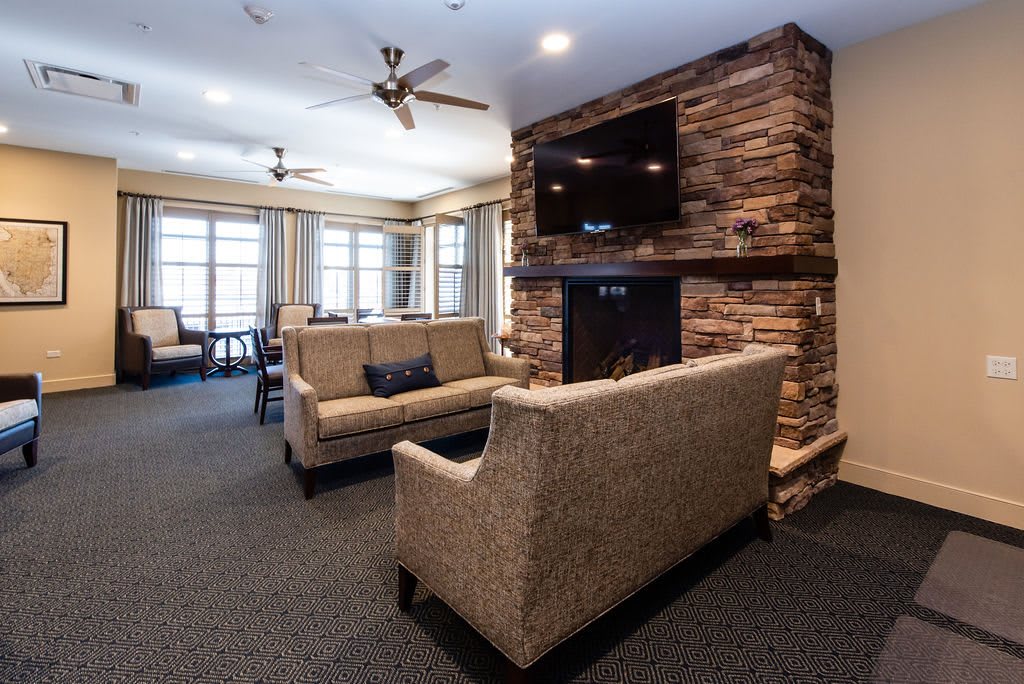 A modern living room featuring a stone fireplace, a mounted television, and comfortable sofas.