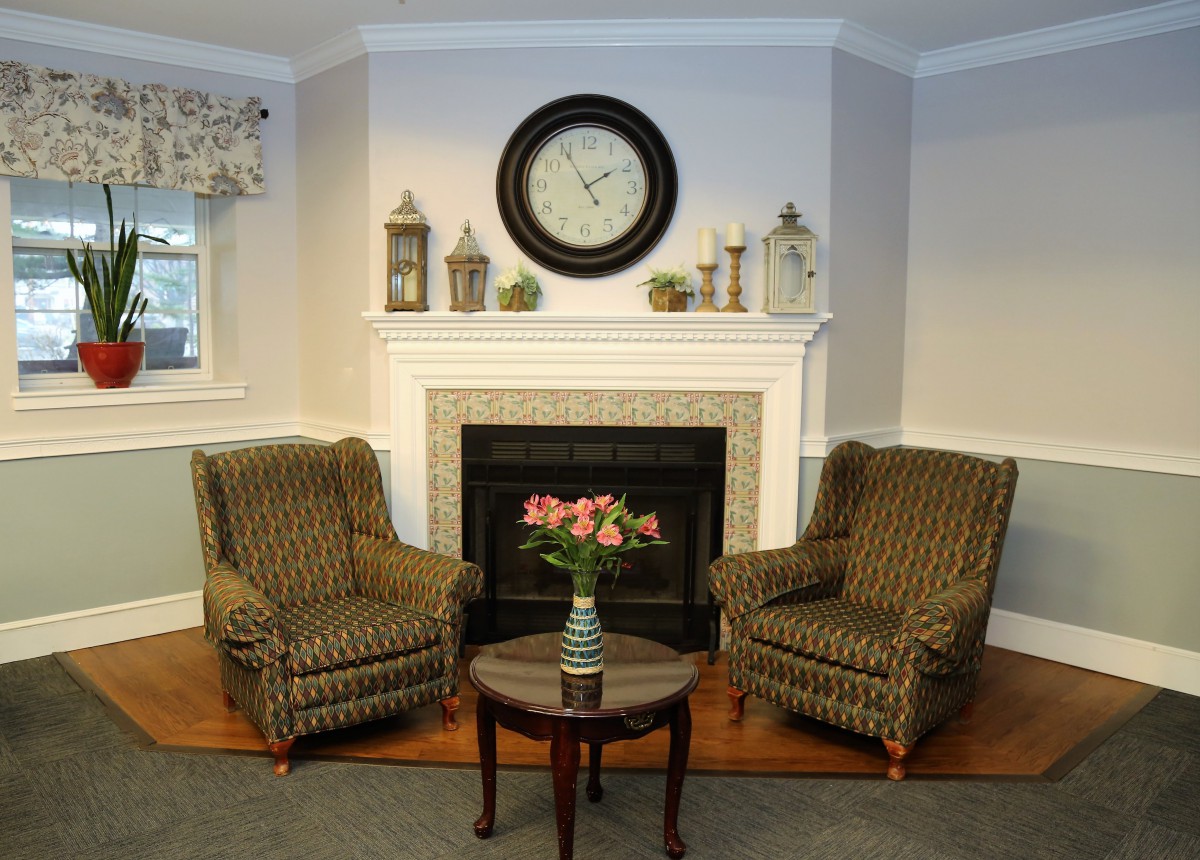 A cozy living room with two armchairs flanking a fireplace, adorned with decorative items and a large wall clock.
