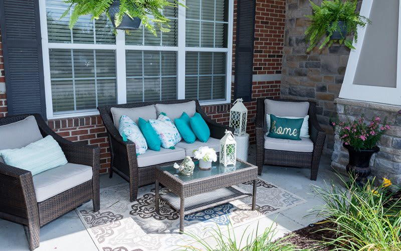 A cozy patio setup with a sofa, armchairs, and decorative pillows, surrounded by greenery.