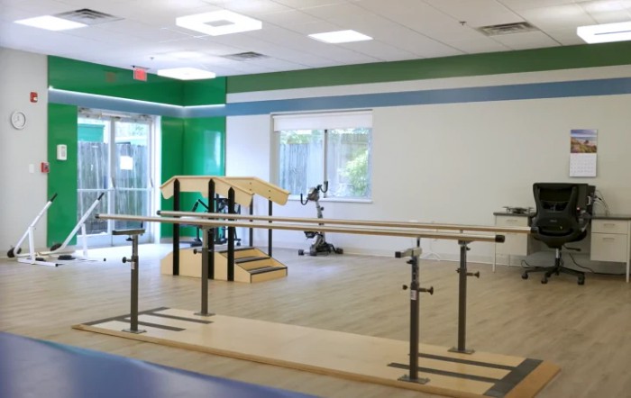 A brightly lit physical therapy room equipped with rehabilitation exercise equipment.