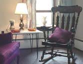 A cozy living room corner with a rocking chair and a small table with a lamp.