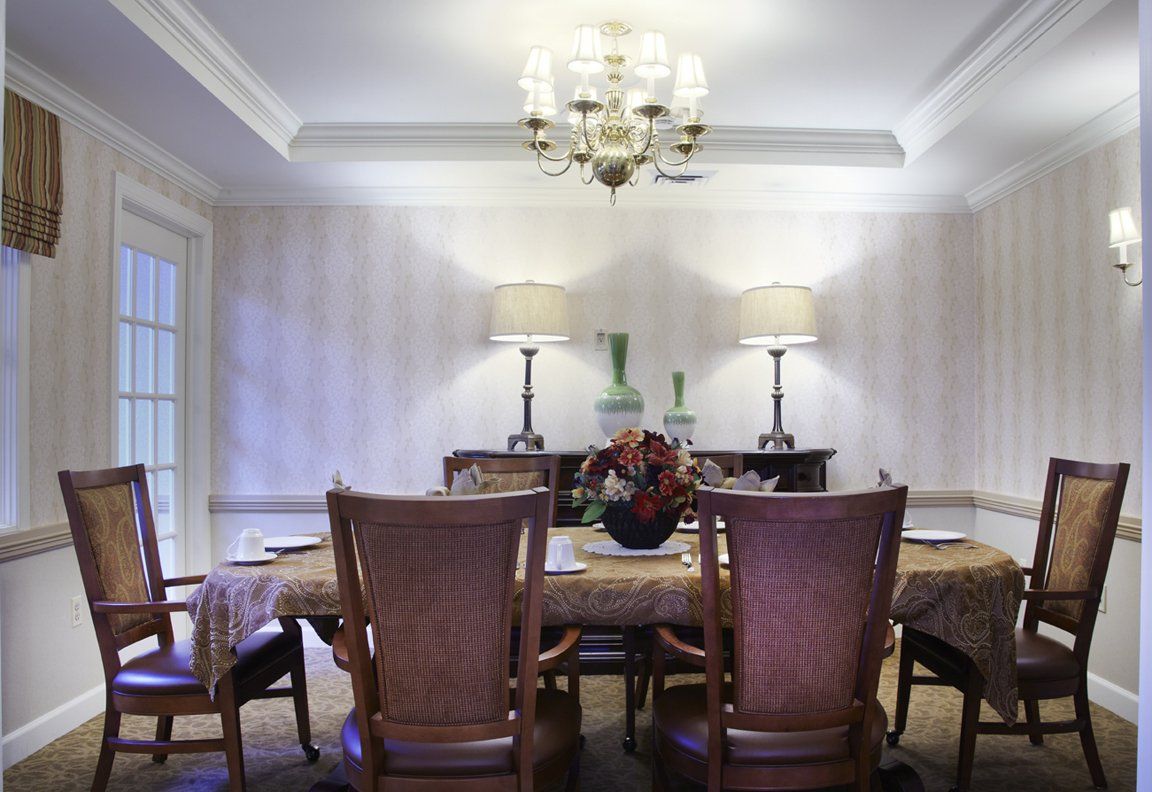 A well-decorated dining room featuring a central table, elegant chairs, and ambient lighting with a chandelier and lamps.