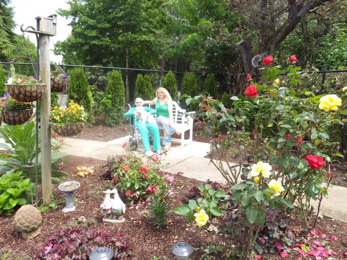 Two people sitting on a bench in a colorful garden surrounded by various flowers.