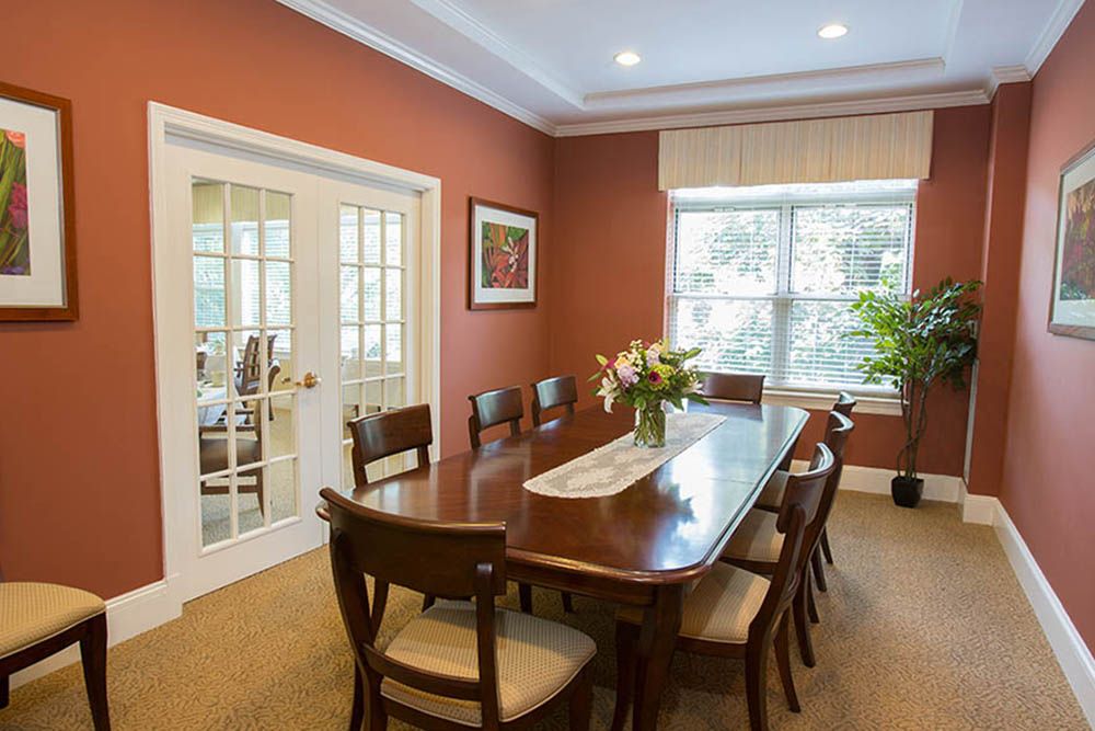 A well-lit dining room with a wooden table, chairs, and flowers on the table.