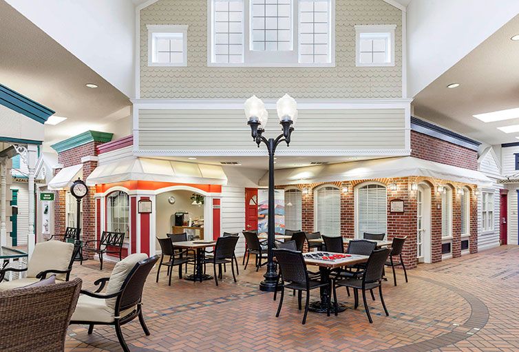 A charming indoor seating area with tables and chairs, featuring decorative streetlamp-style lighting against a backdrop of house-like architecture and brick walls.