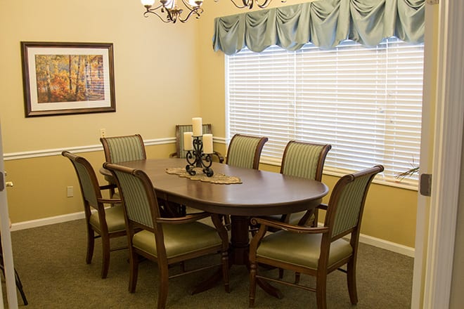 A cozy dining room with a wooden table and six upholstered chairs, decorated with candles and lit by a chandelier.