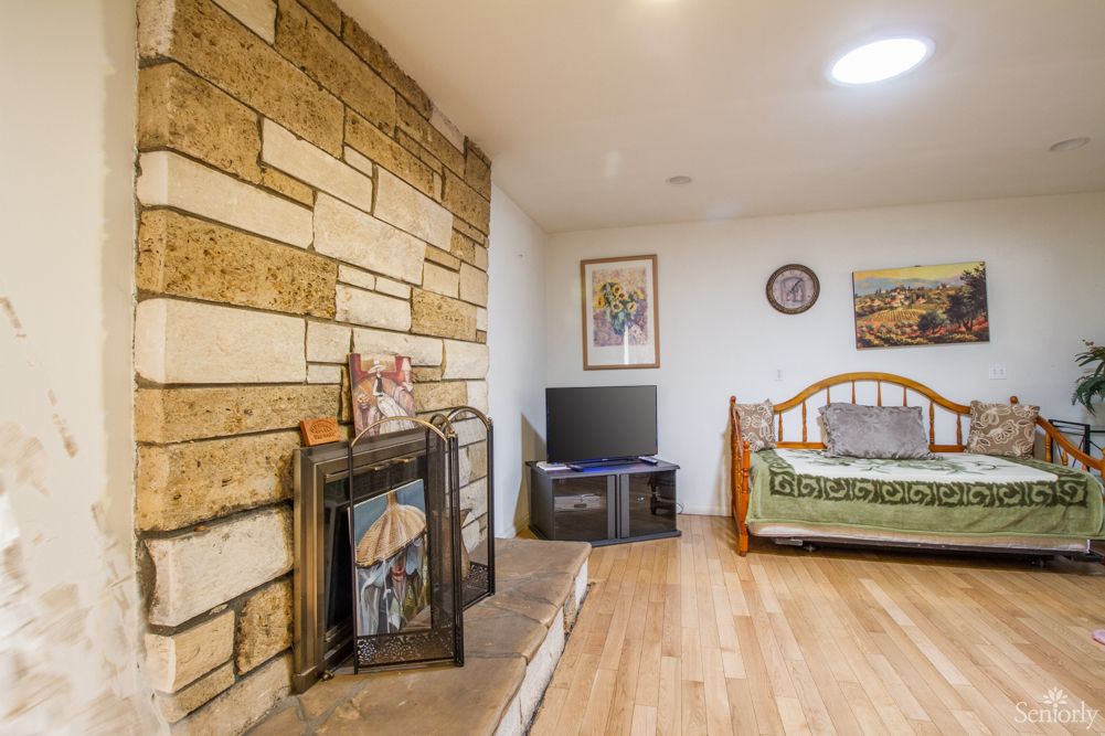 A cozy living area featuring a stone wall with a fireplace, a television on a stand, and a bed with decorative artwork on the walls.