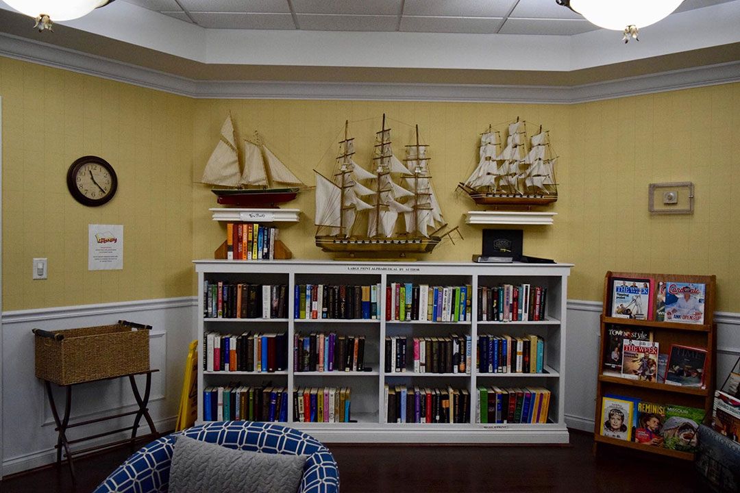 A cozy living room featuring a bookshelf filled with colorful books and decorated with model ships.