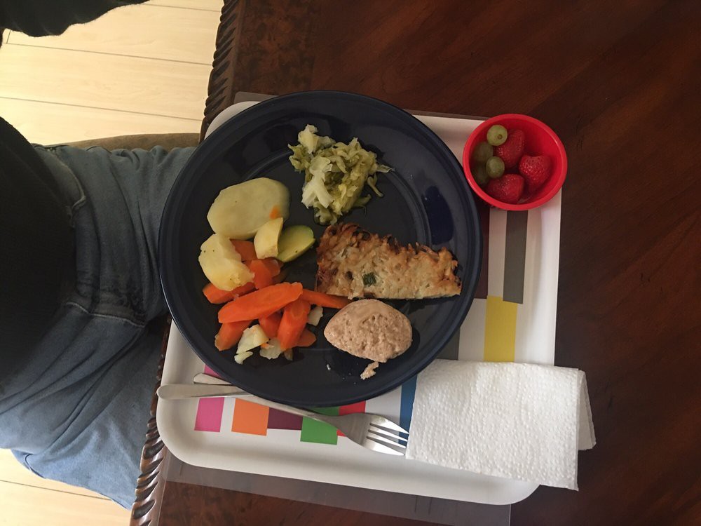 A meal served on a tray with fish, potatoes, mixed vegetables, and cherry tomatoes.