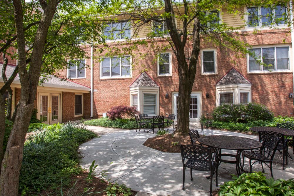 A peaceful courtyard with outdoor seating surrounded by a brick building and lush greenery.