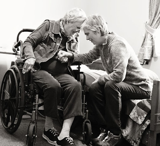 A caregiver tenderly assists an elderly woman in a wheelchair, highlighting the compassion in elder care.