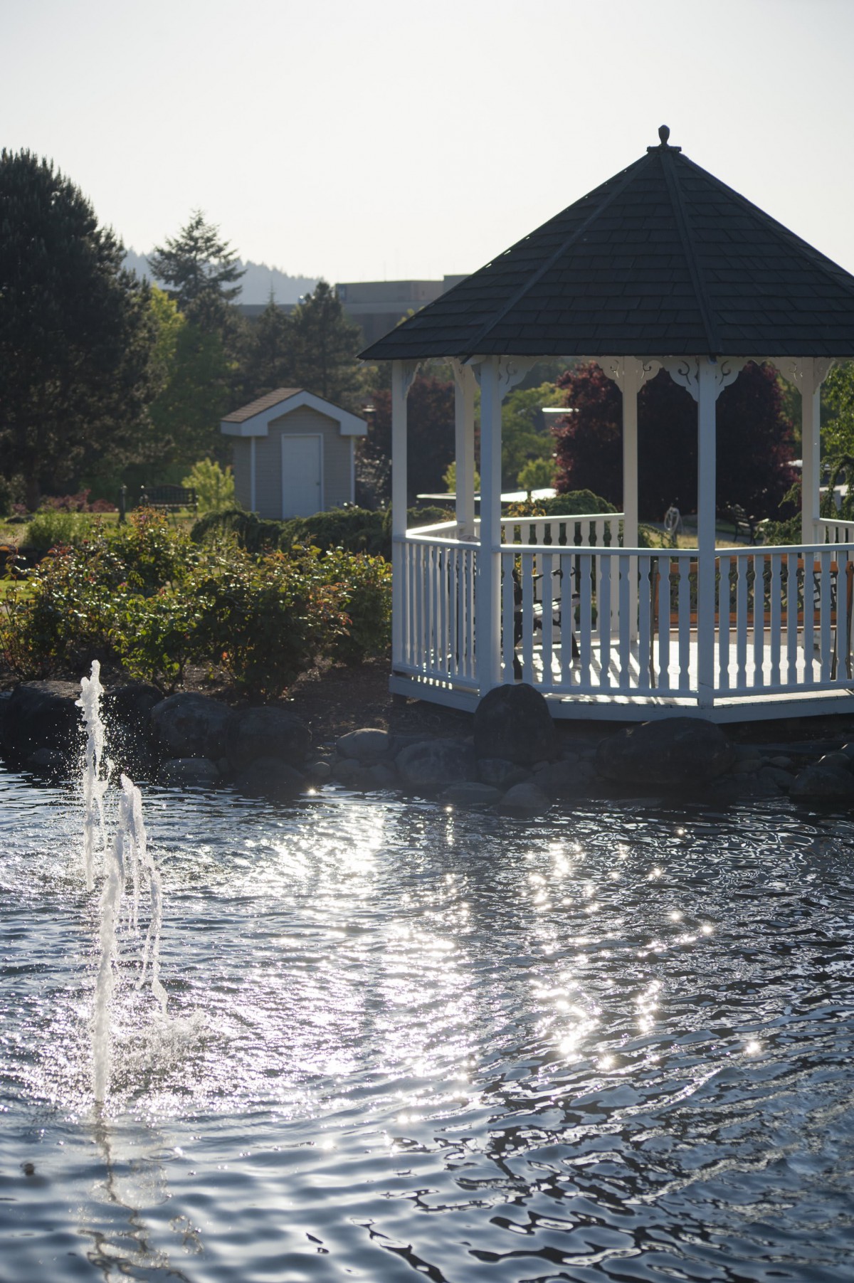 A serene garden scene with a gazebo overlooking a pond with a fountain.