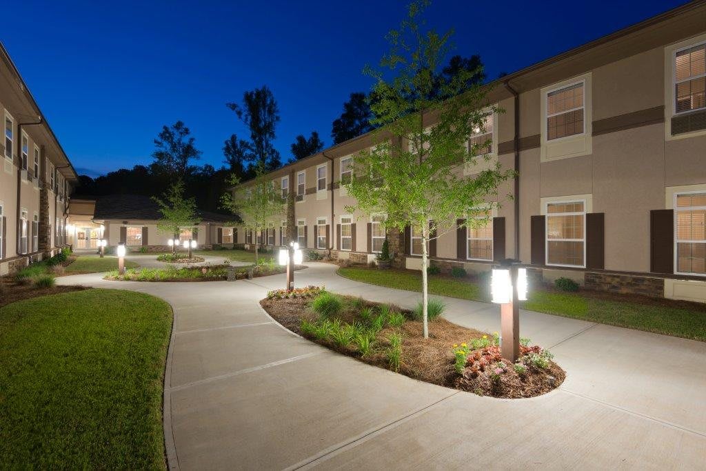 A well-lit residential building with a landscaped pathway at night.