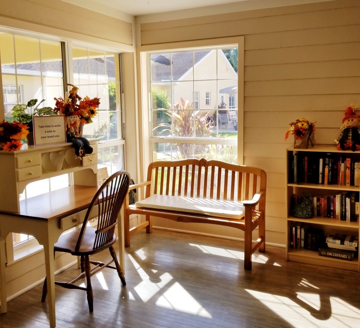 A cozy, sunlit room with a wooden desk, chair, and bench.