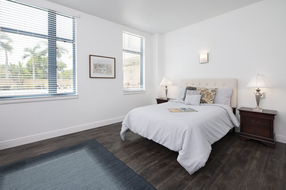 A modern, minimalist bedroom with white walls and hardwood floors, featuring a neatly made bed and stylish decor.