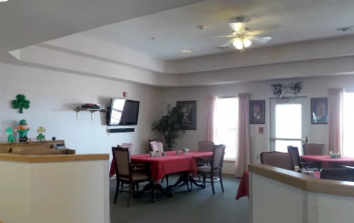 A dining area with a table and chairs, featuring a wall-mounted television and a ceiling fan.