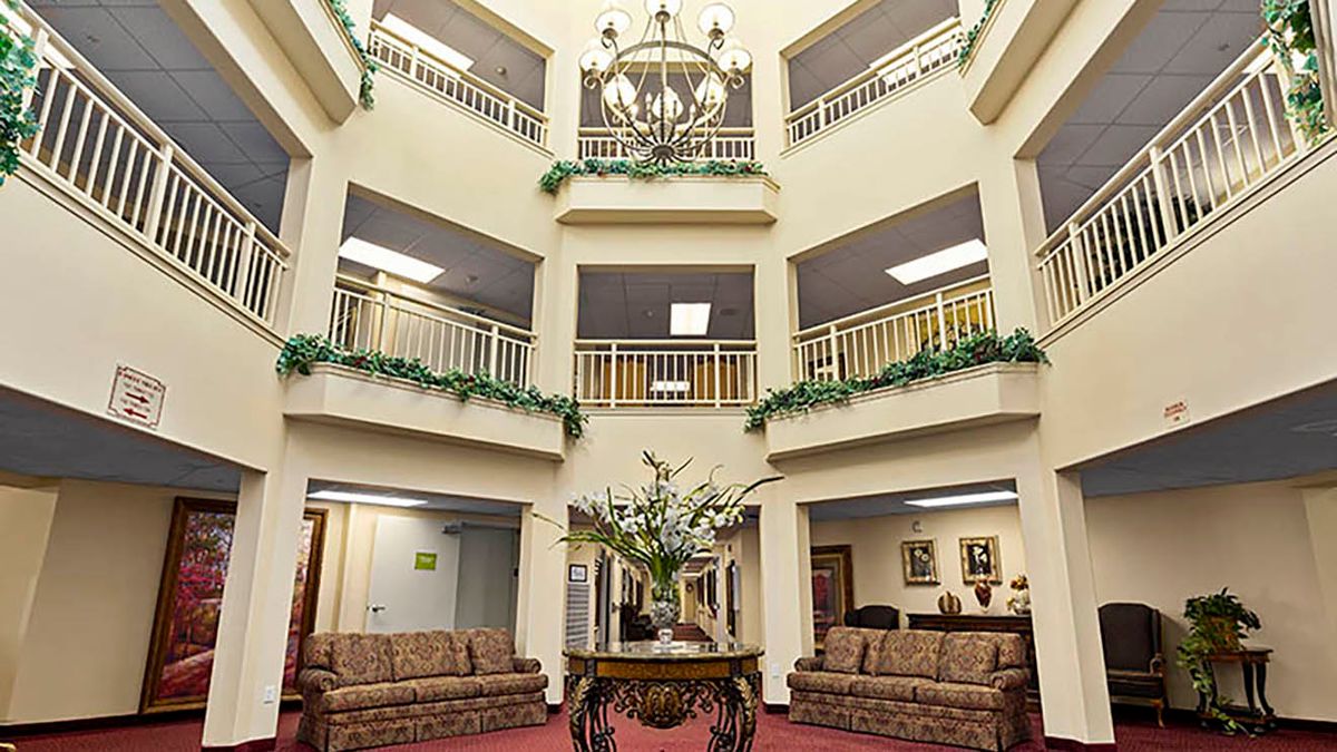 A spacious lobby area featuring a central table with floral decorations, surrounded by multiple floors and balconies adorned with greenery.