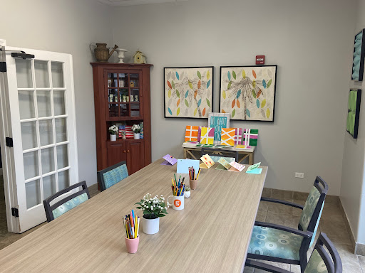 A well-organized workspace featuring a large table, decorative art, and supplies for creative activities.
