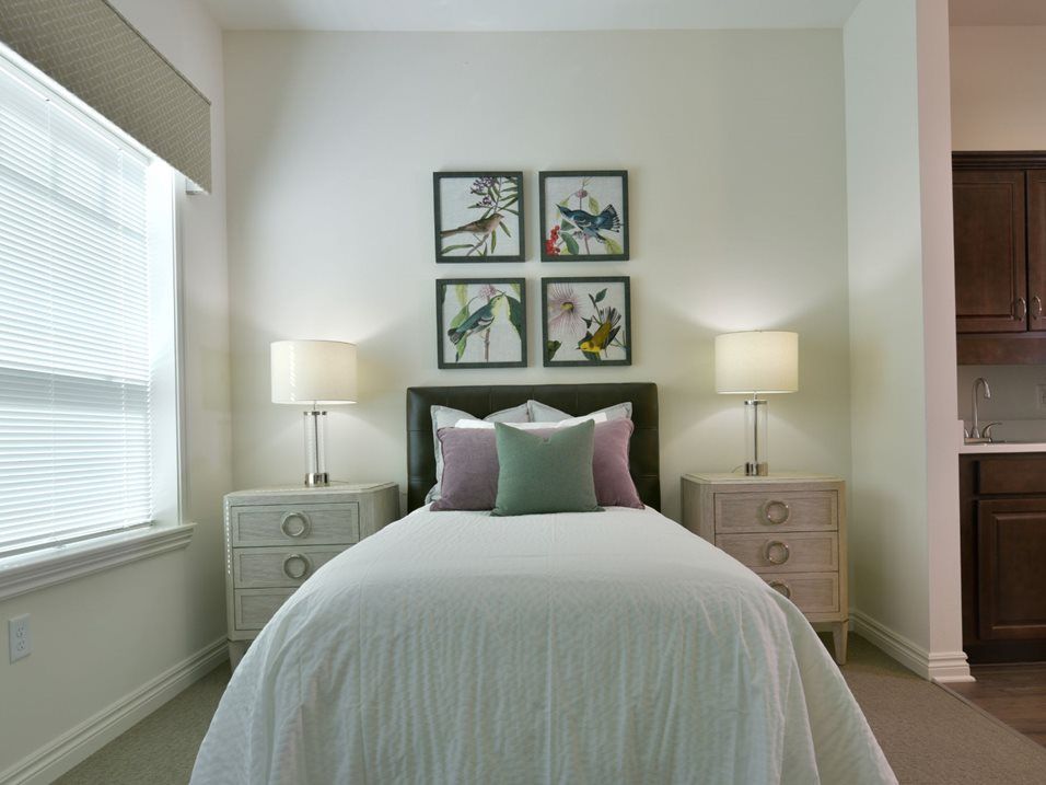 A neatly arranged bedroom with a bed, flanked by two lamps, and wall artwork above the headboard.