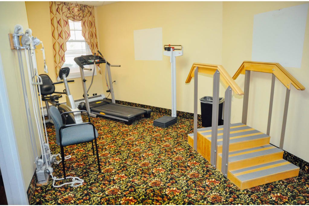 A small indoor exercise room featuring a treadmill, stationary bike, and scale on a carpeted floor.